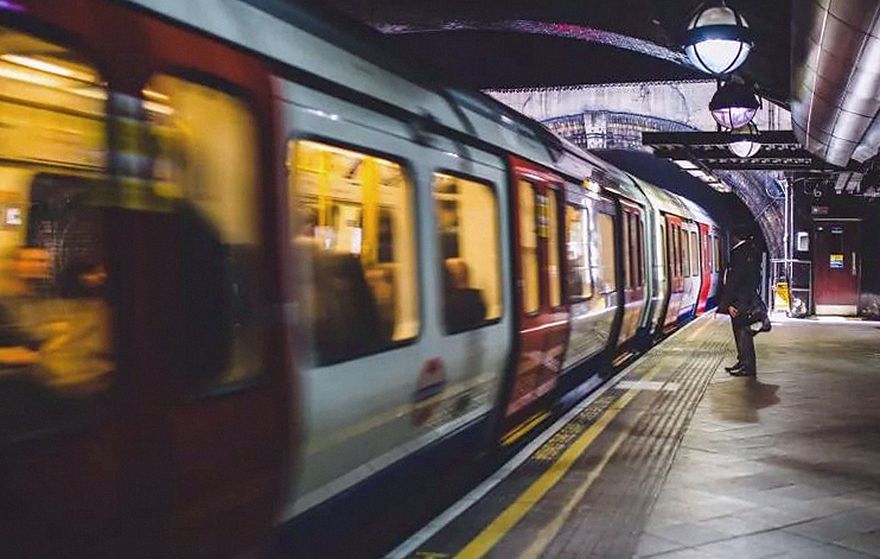 Andén de metro con un tren en movimiento y un viajero esperando